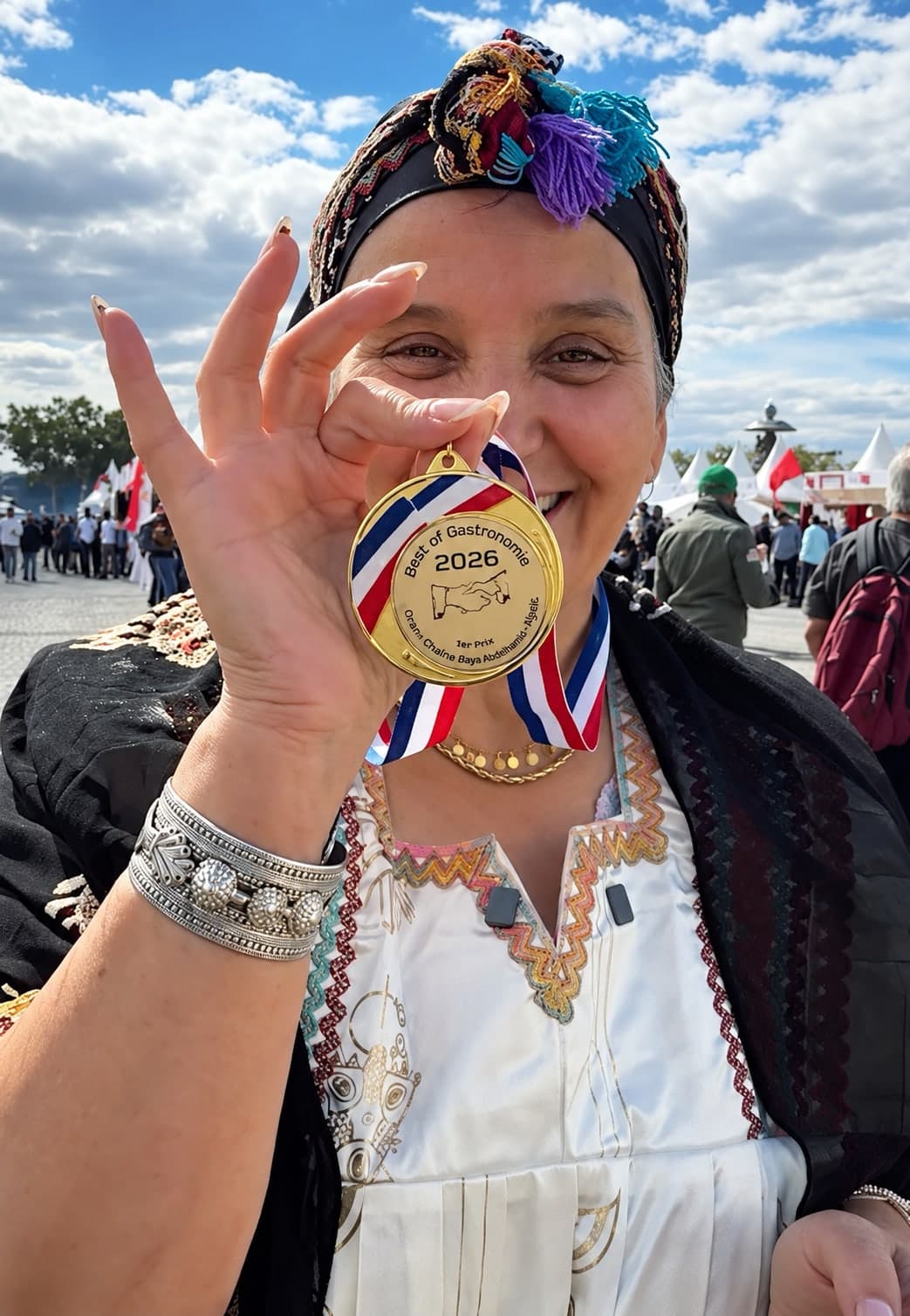 Nna Nora sourit en montrant sa médaille d’or Best of Gastronomie 2026, en tenue kabyle brodée.